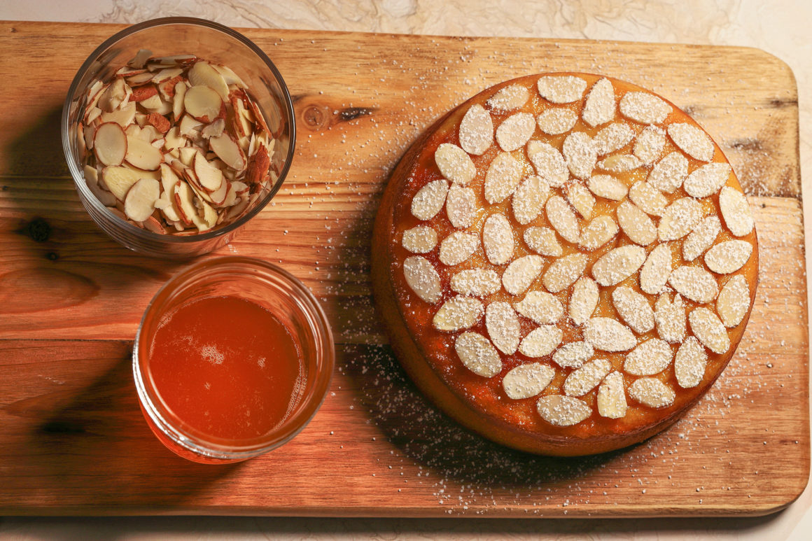 cake on cutting board with syrup and almonds